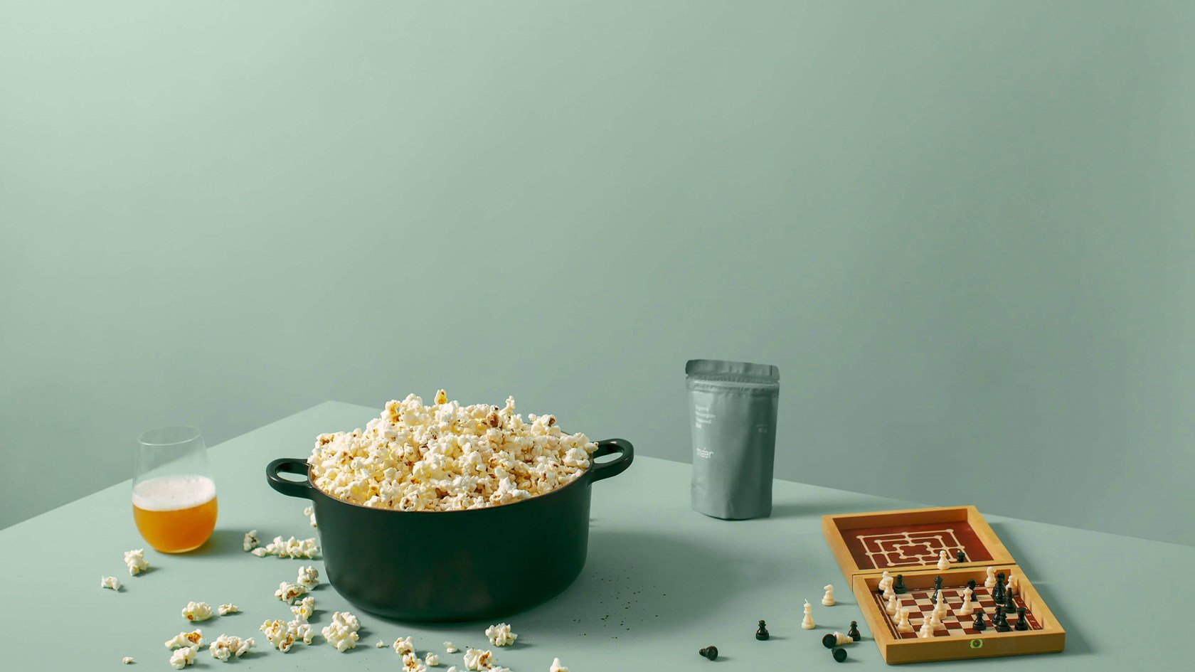 Popcorn in a bowl on a table with scattered pieces of popcorn and chess pieces